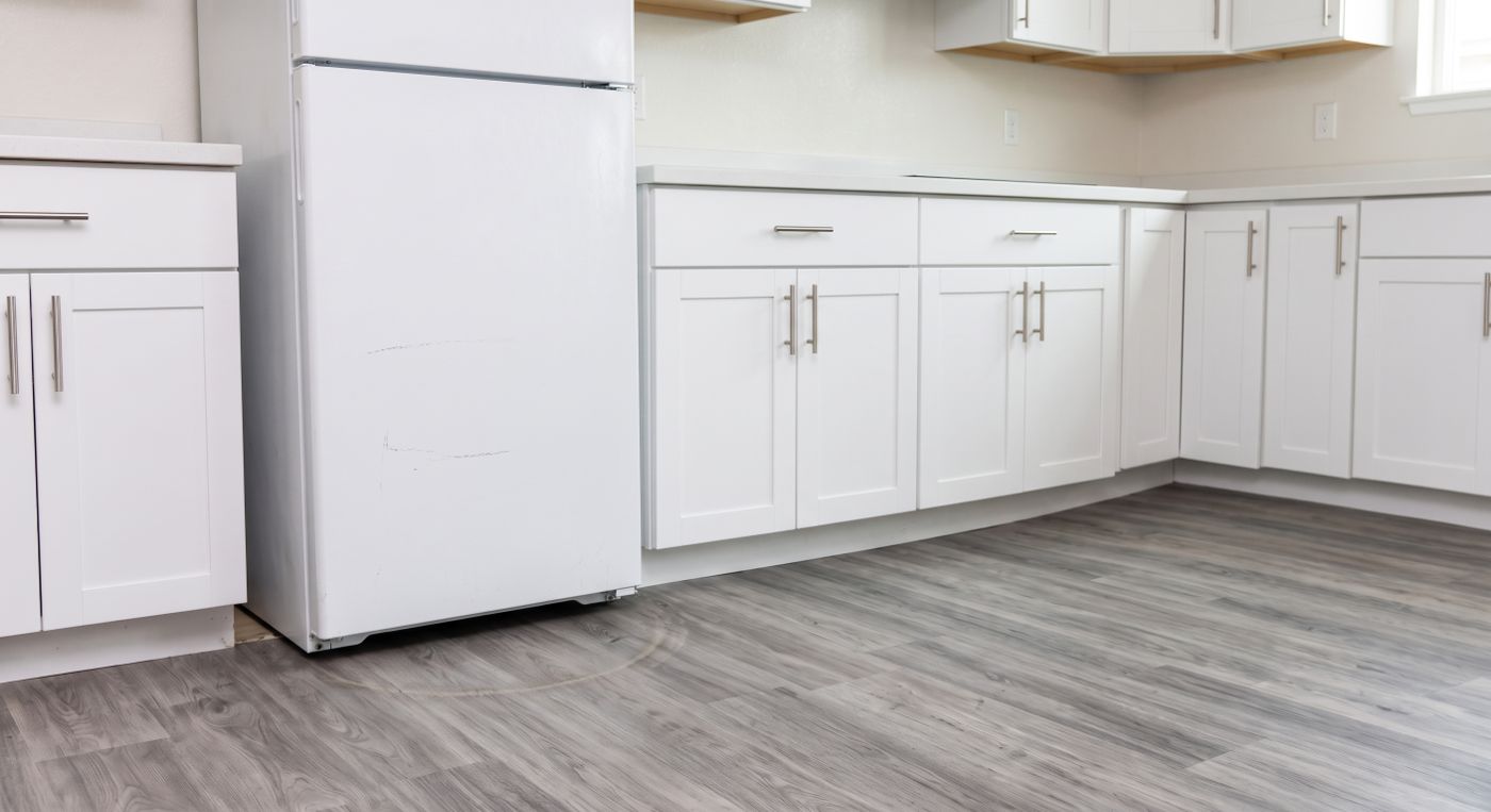 White top-freezer refrigerator pulled out from its kitchen alcove, scuffed and awaiting service