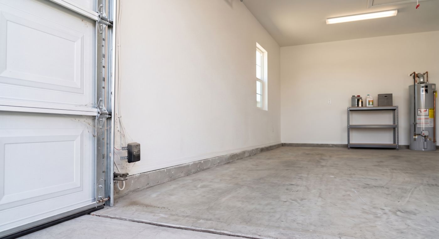 Empty garage with a safety sensor sitting loose and off-square on its bracket beside the door track