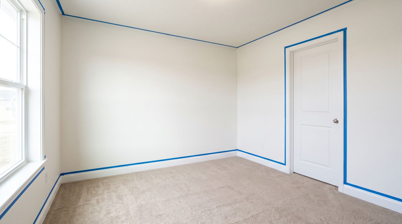 The same bedroom with clean, freshly painted walls and blue painter's tape still masking the baseboards, ceiling line, and door casing