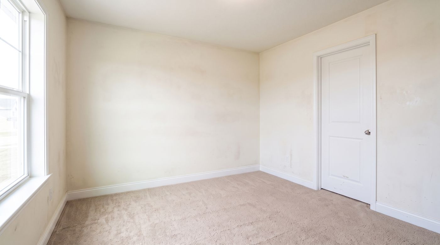 Empty bedroom with yellowed walls marked by scuffs, smudges, and patched spots left after a tenant moved out